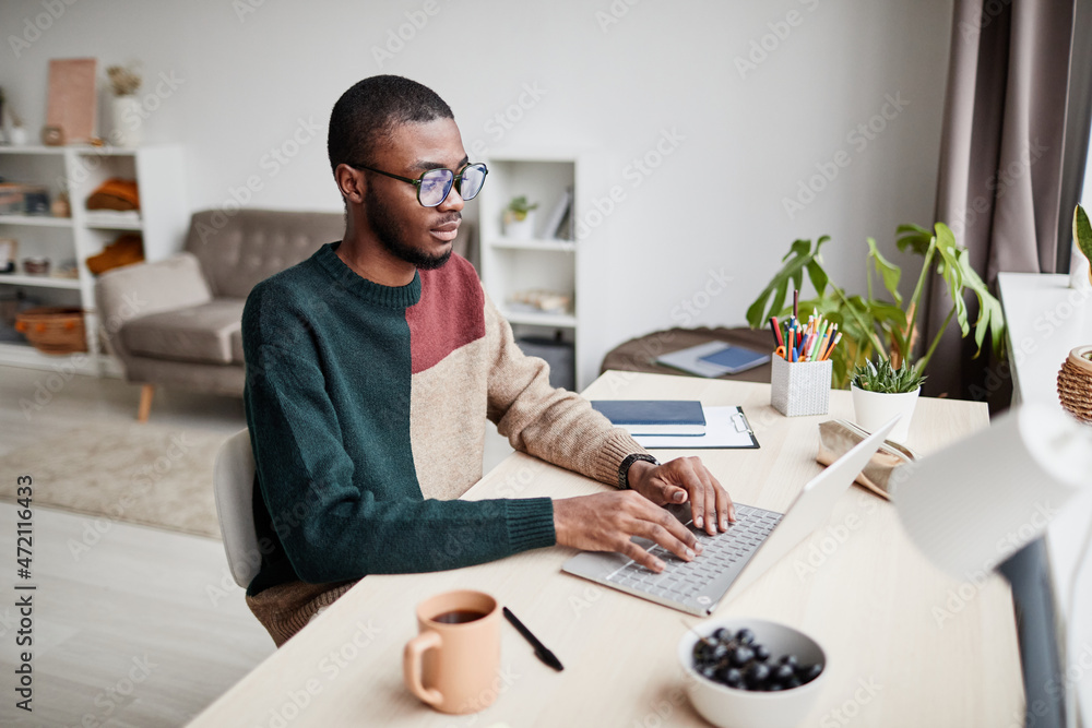 Career Goldmine African-American man wearing glasses while working from home and using laptop, copy space