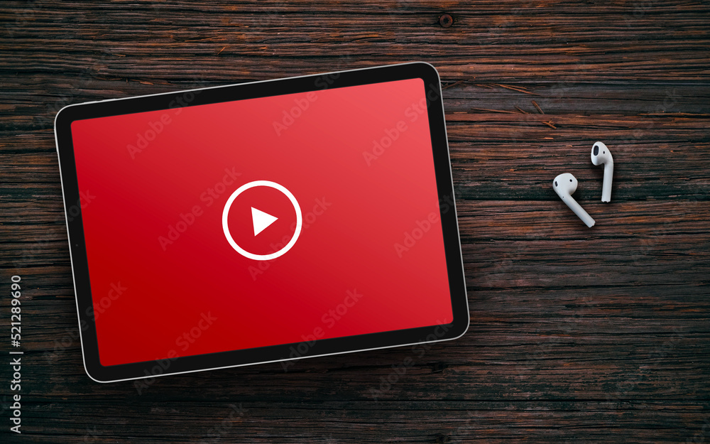 Play button on red screen of tablet and wireless earphones on dark wooden surface