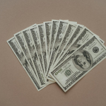 A neat arrangement of US dollar banknotes laid out in a fan shape on a brown surface.